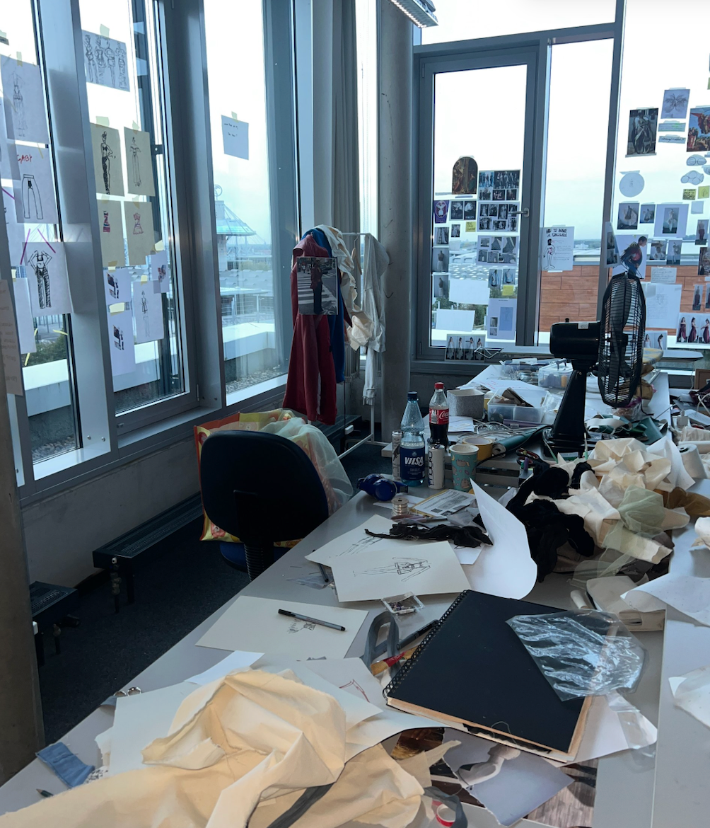 Blick in Stylianis Atelier: Modeskizzen am Fenster, Moodboard und Stoffproben auf dem Arbeitstisch