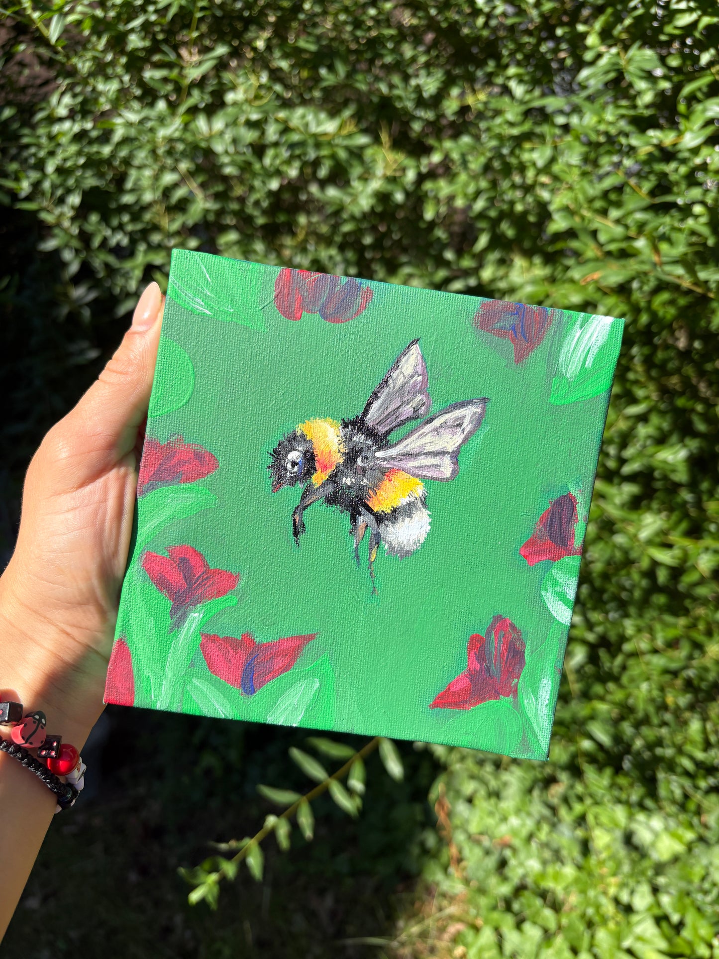 Handgemaltes Acrylbild 'Bien-Melissa': Biene zwischen Mohnblumen auf grünem Grund, 15×15 cm Leinwand, in der Hand gehalten vor grünem Hintergrund