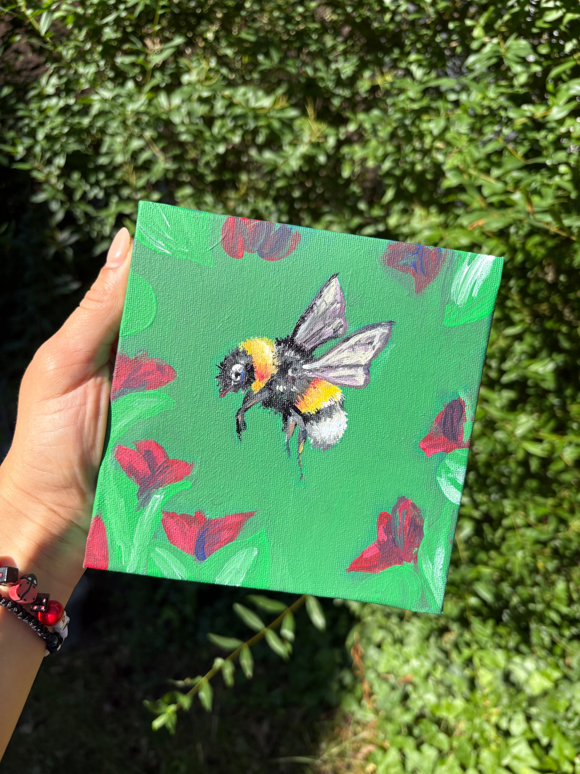 Handgemaltes Acrylbild 'Bien-Melissa': Biene zwischen Mohnblumen auf grünem Grund, 15×15 cm Leinwand, in der Hand gehalten vor grünem Hintergrund